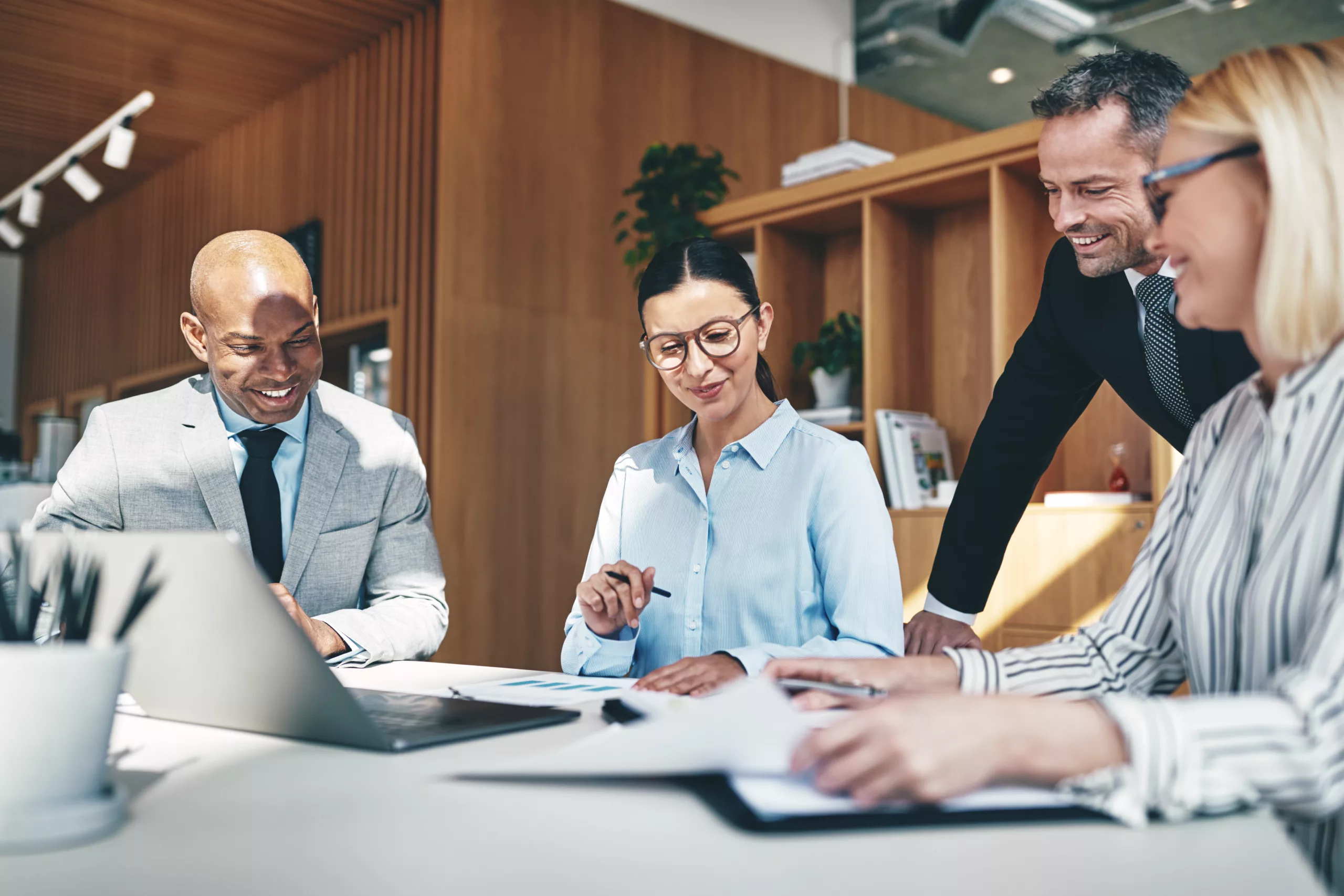 Diverse group of businesspeople laughing while going over paperwork together during a meeting at a boardroom table in an office